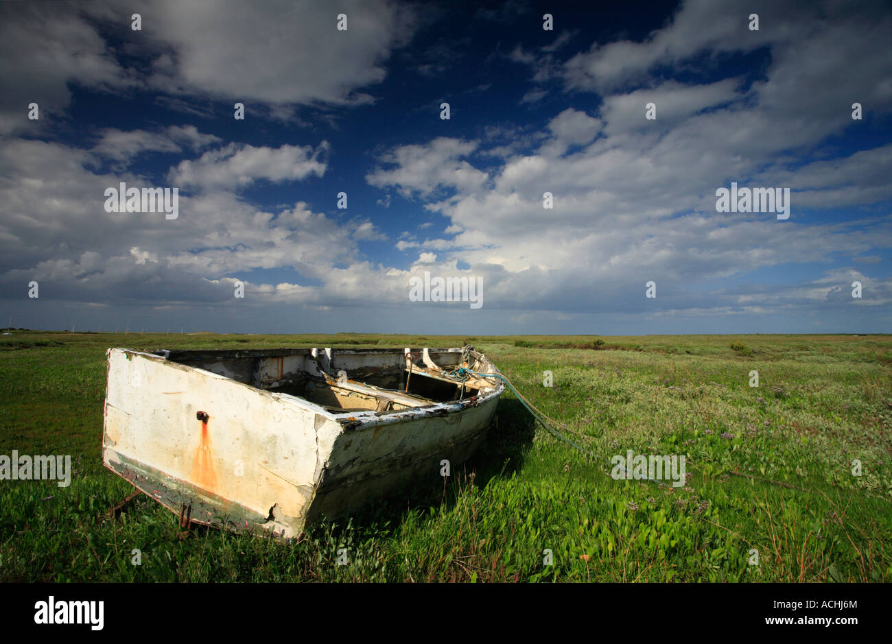 Old wooden rowing boat resting on the saltmarsh at Brancaster Staithe under a blue sky with white clouds. Stock Photo