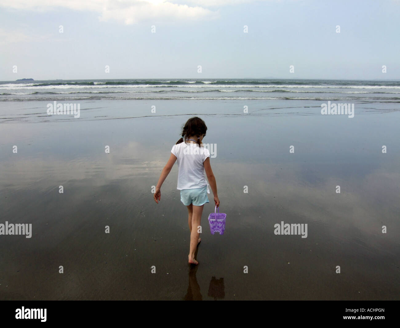 Girl walking out to the sea carrying a bucket, UK Stock Photo