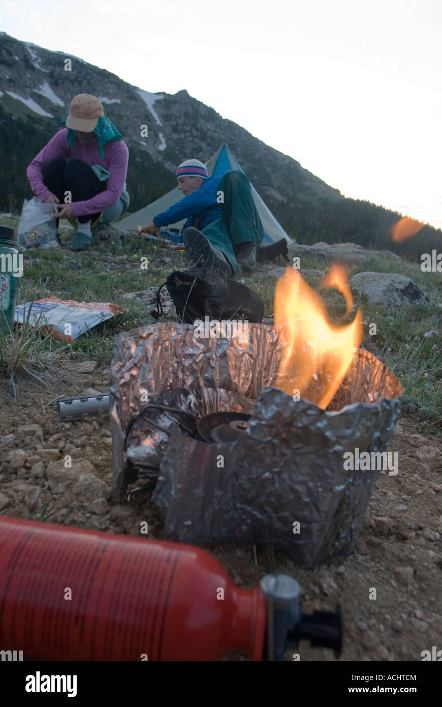 MSR camping stove priming while two campers sit in the campsite Stock