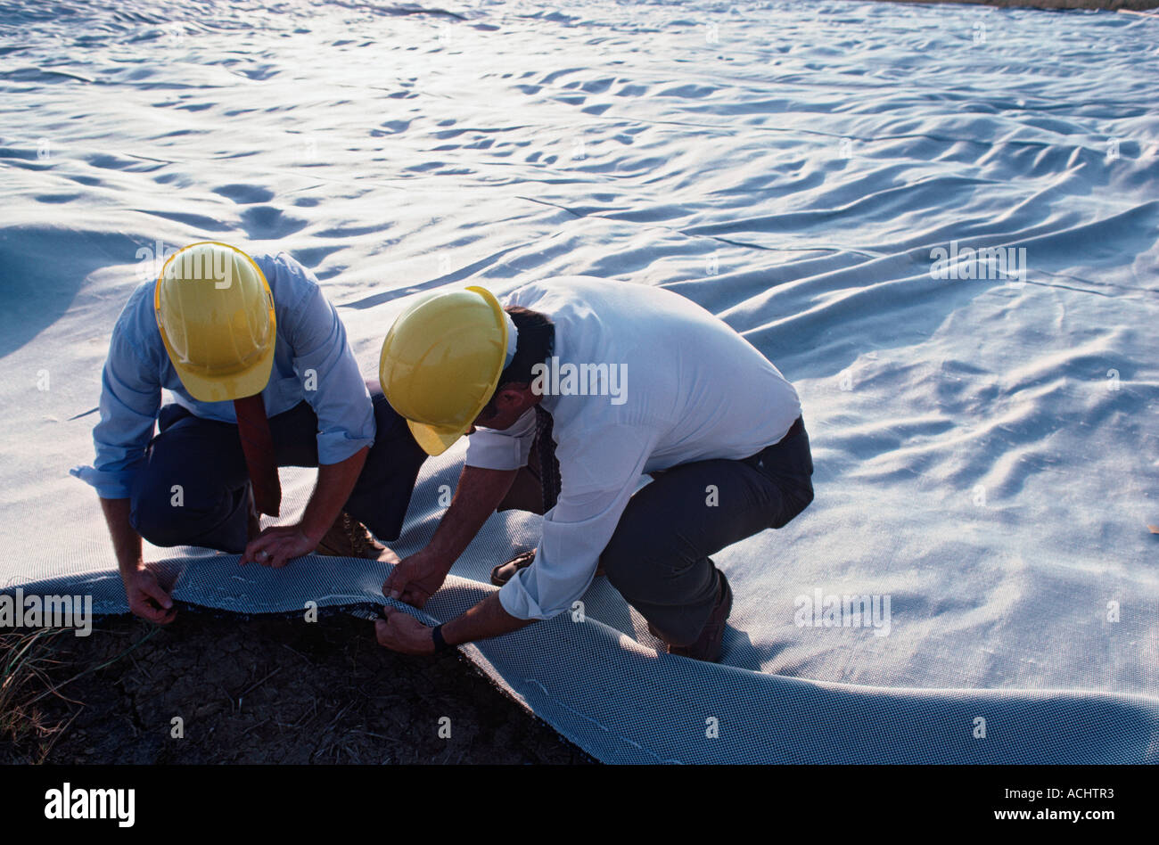 Two engineers lay waterpermeable fabric to prevent soil erosion Stock