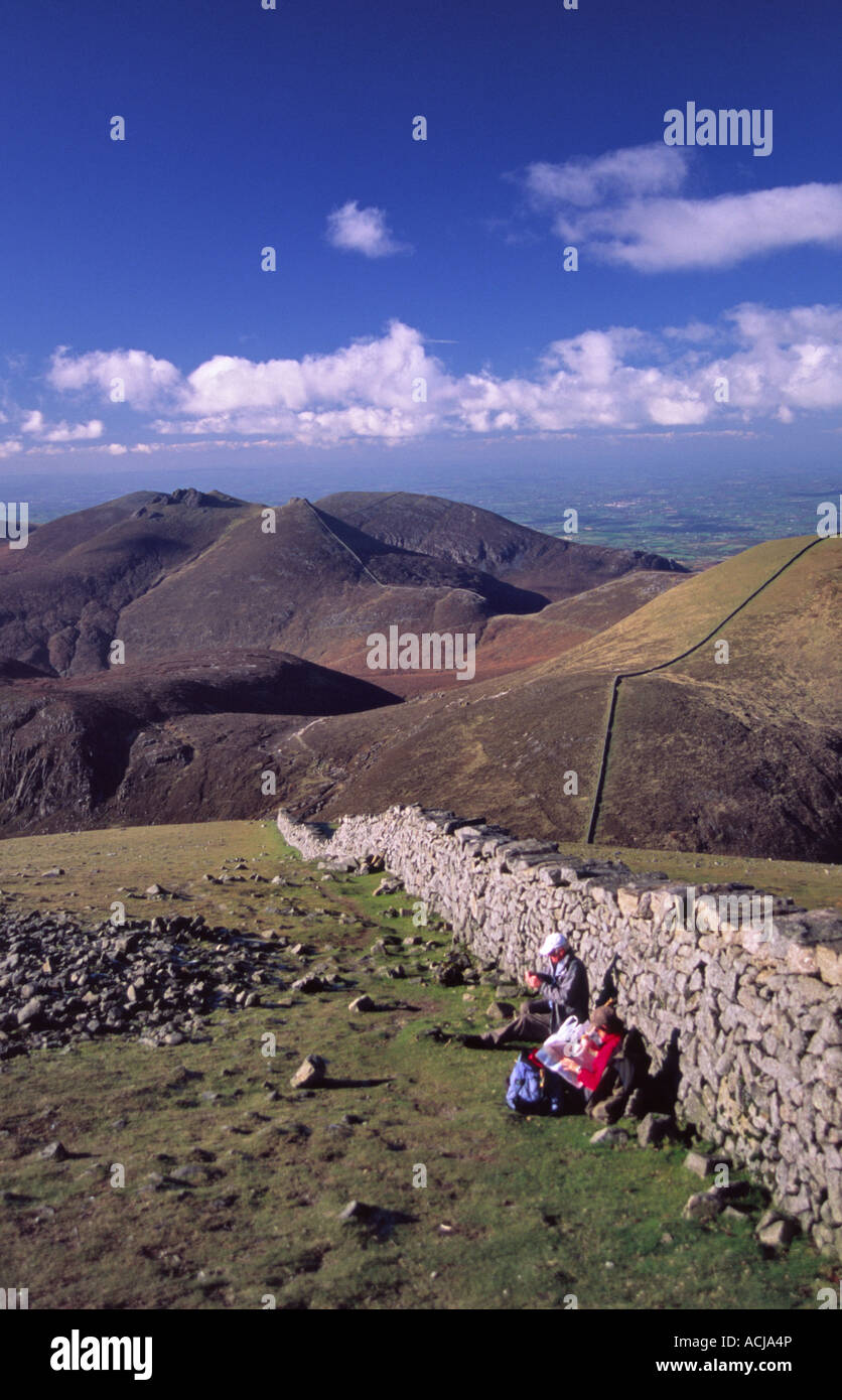 Walkers resting beside the Mourne Wall at the summit of Slieve Donard, Mourne Mountains, County Down, Northern Ireland. Stock Photo