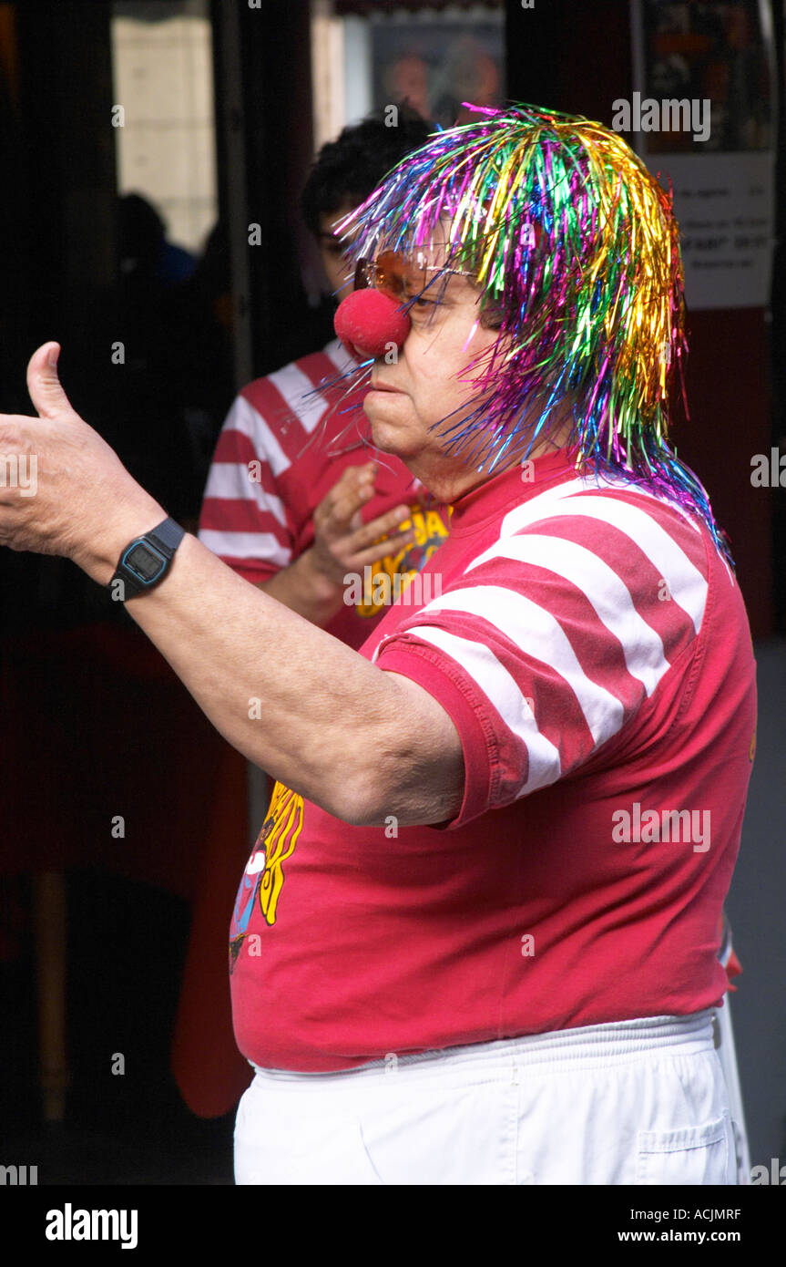A street comedian dressed up as a clown with a wig false hair in coloured metal stripes and a big red round nose, in the restaurant El Palenque, the sword fish swordfish, in the Mercado del Puerto, the market in the port harbour harbor where many people go and eat and shop on weekends Montevideo, Uruguay, South America Stock Photo