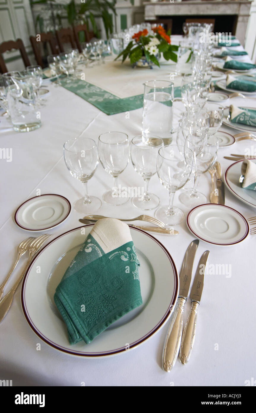 The magnificent lunch table set in traditional style with starched linen  table cloth, white plates with golden decoration, silverware knives and  forks, white and green linen napkins and many glasses for tasting