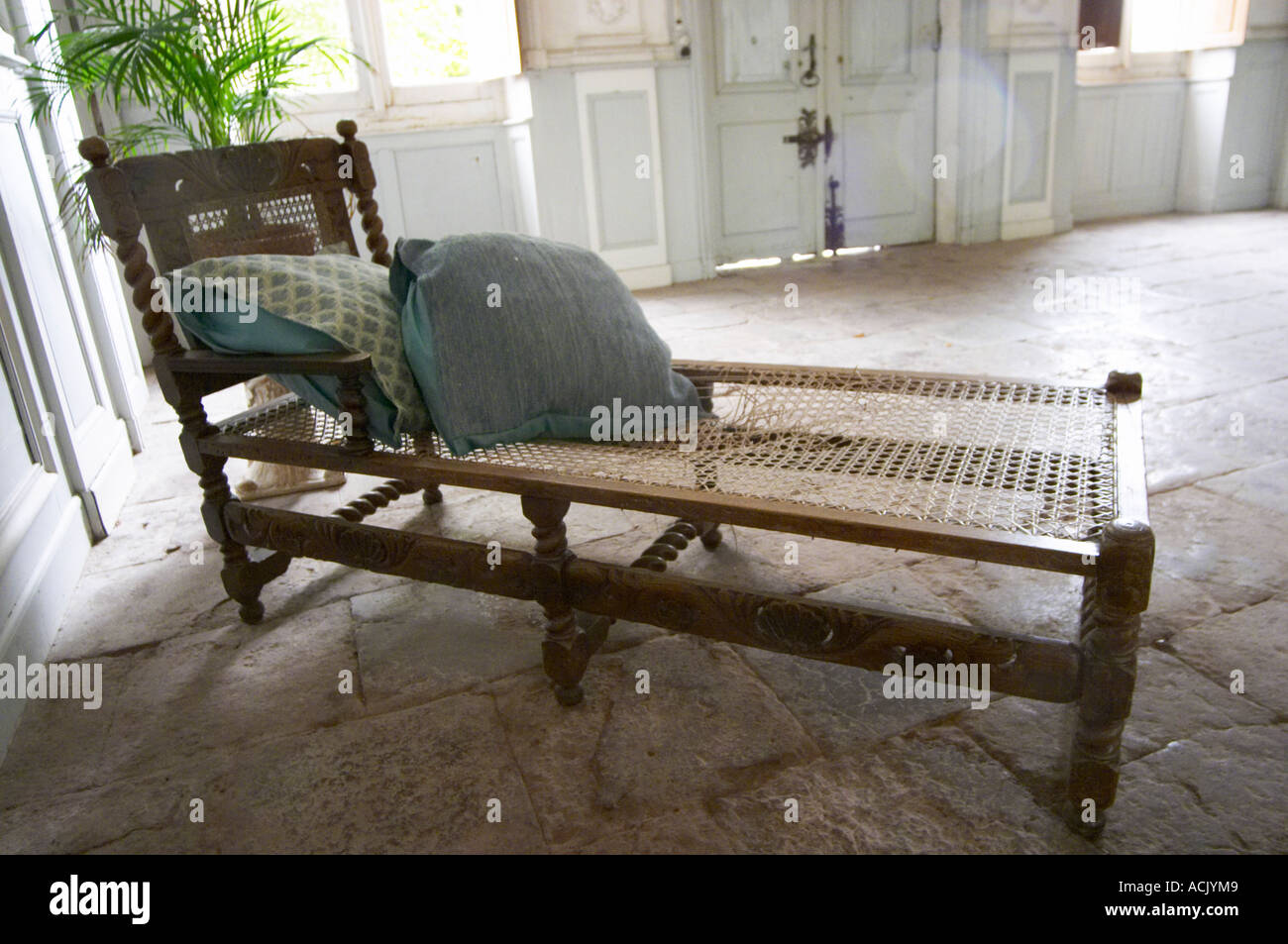 In the stately entrance hall: An old lounging chair chaise longue with a plant on the stone floor, walls painted white and soft Stock Photo