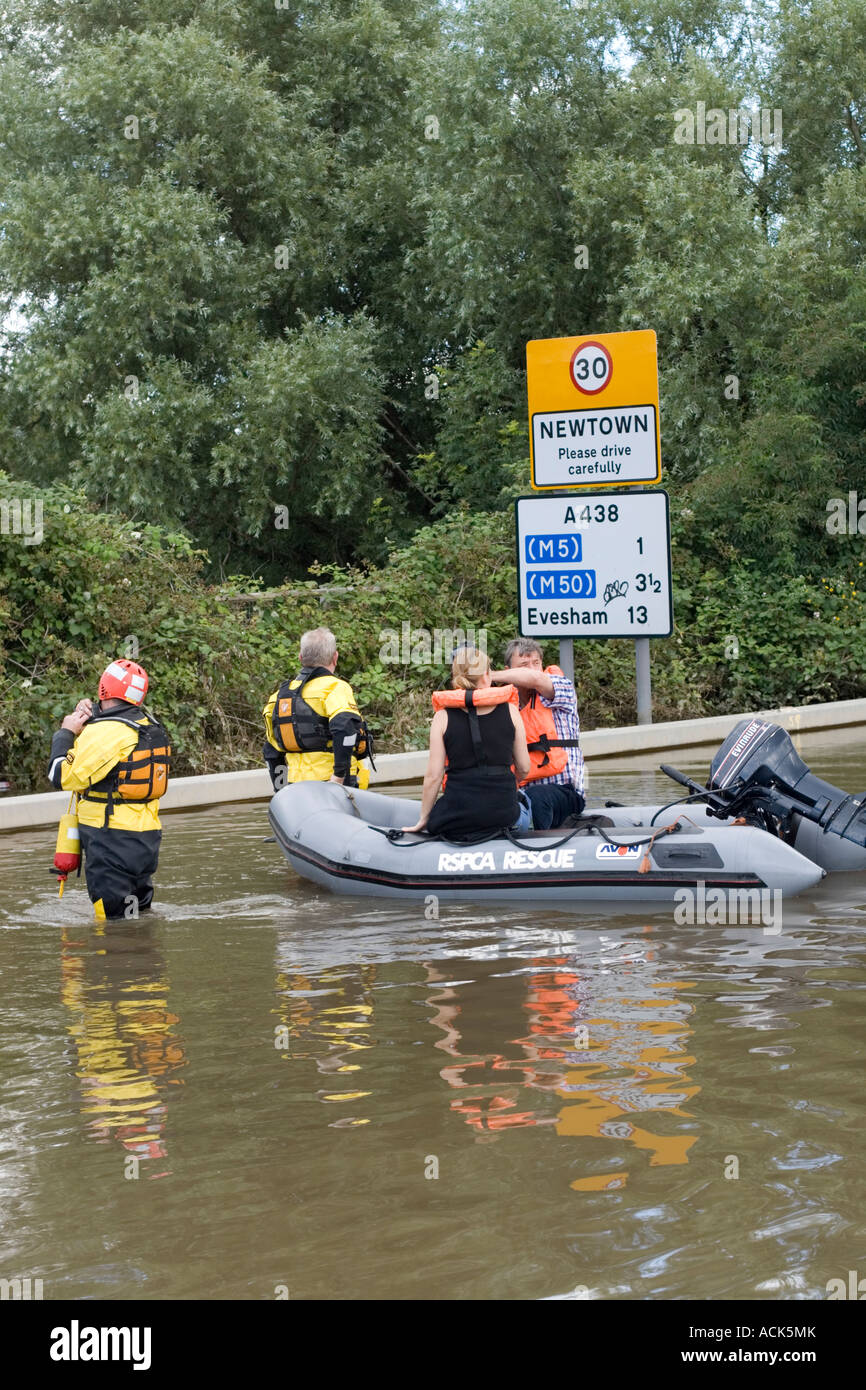 Man and woman with shopping in inflatable rubber dinghy near drive carefully road sign on flooded road  Tewkesbury UK July 2007 Stock Photo