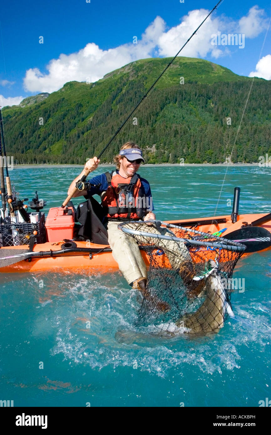 Male fishreman sitting on edge of kayak catching a halibut in
