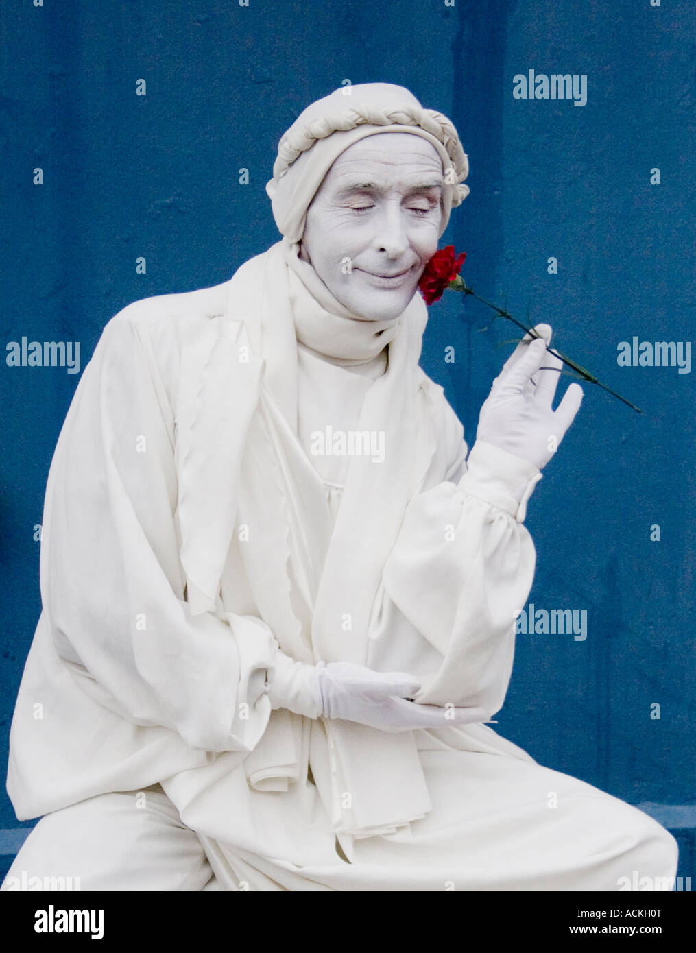 Mime artist wearing white robes, and with white face smelling a red rose Stock Photo