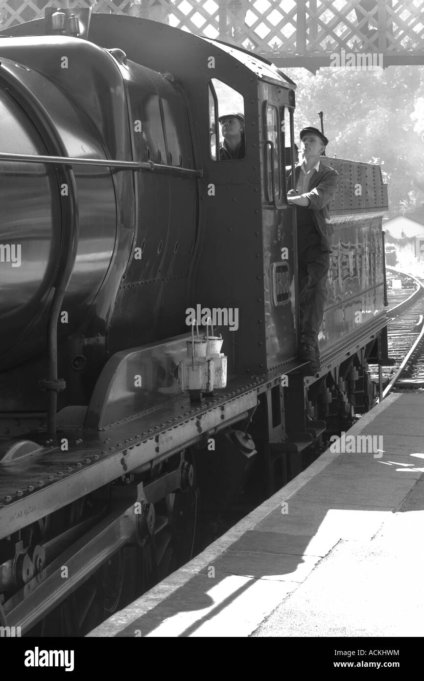 A black & white image of a steam train and the engineers in a station ...
