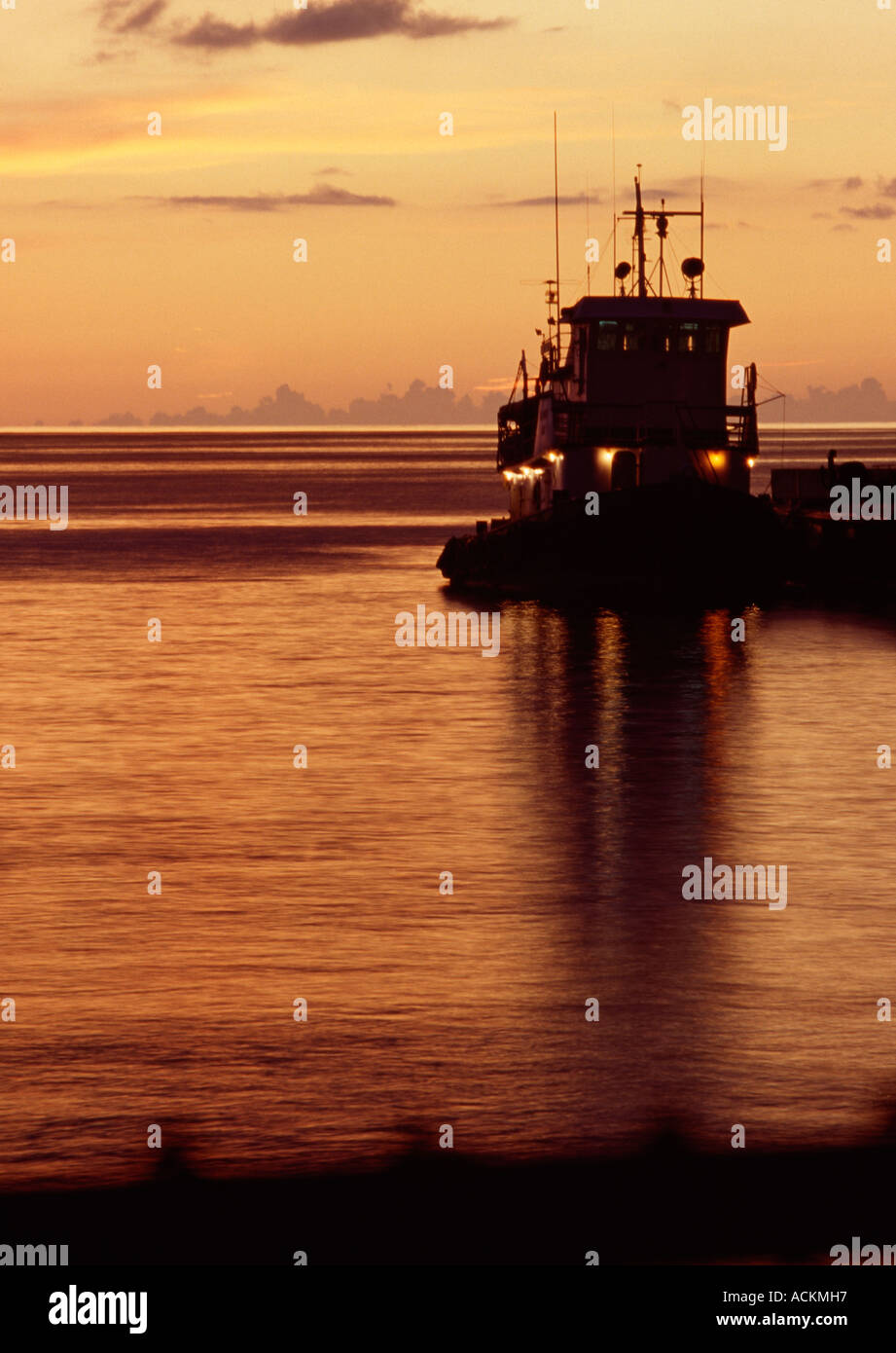 Grand Cayman Cayman Islands Georgetown Harbor tugboat in silhouette after sunset golden skies Stock Photo