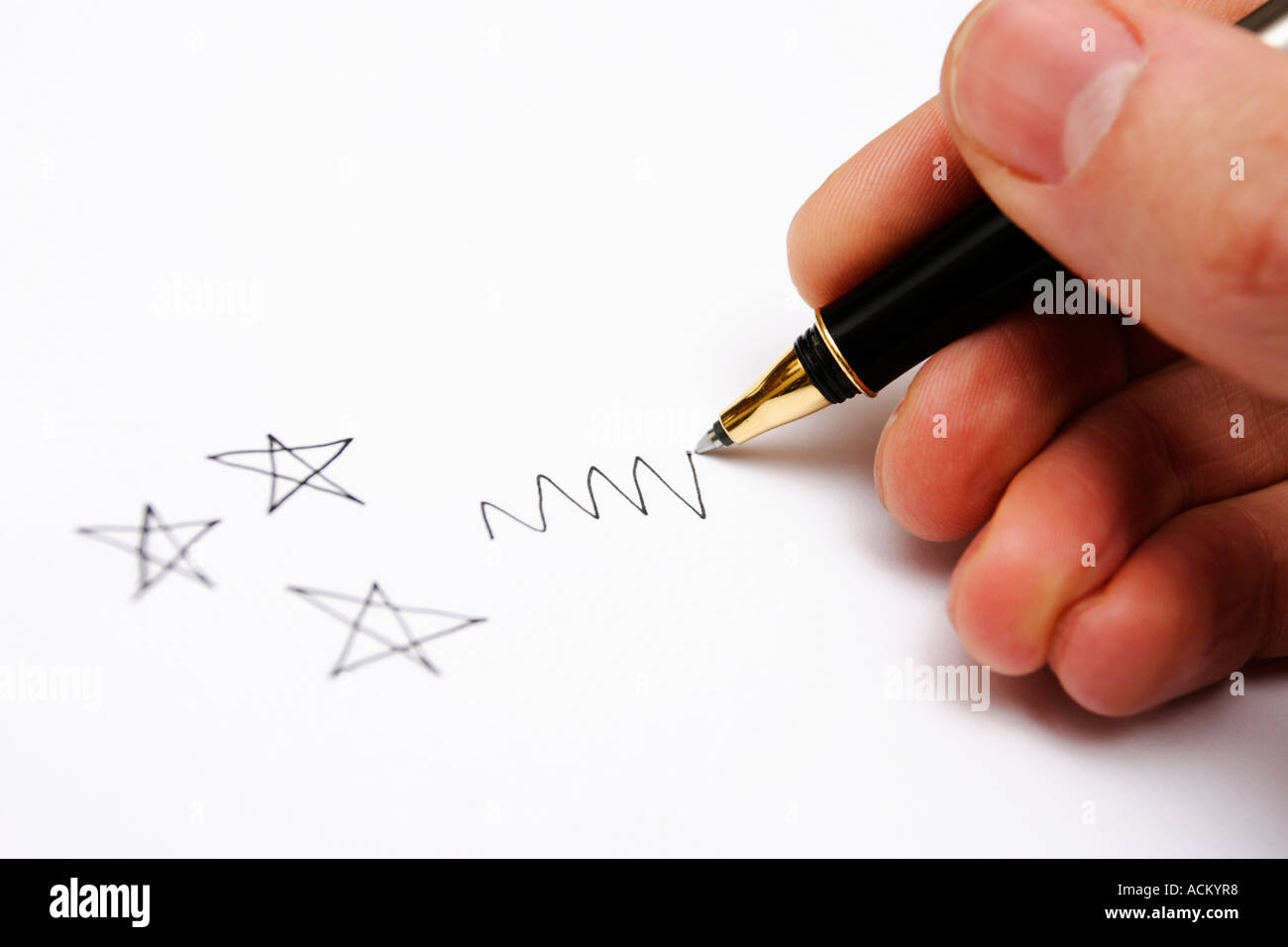 A man's hand doodling stars and a squiggle with a black pen Stock Photo