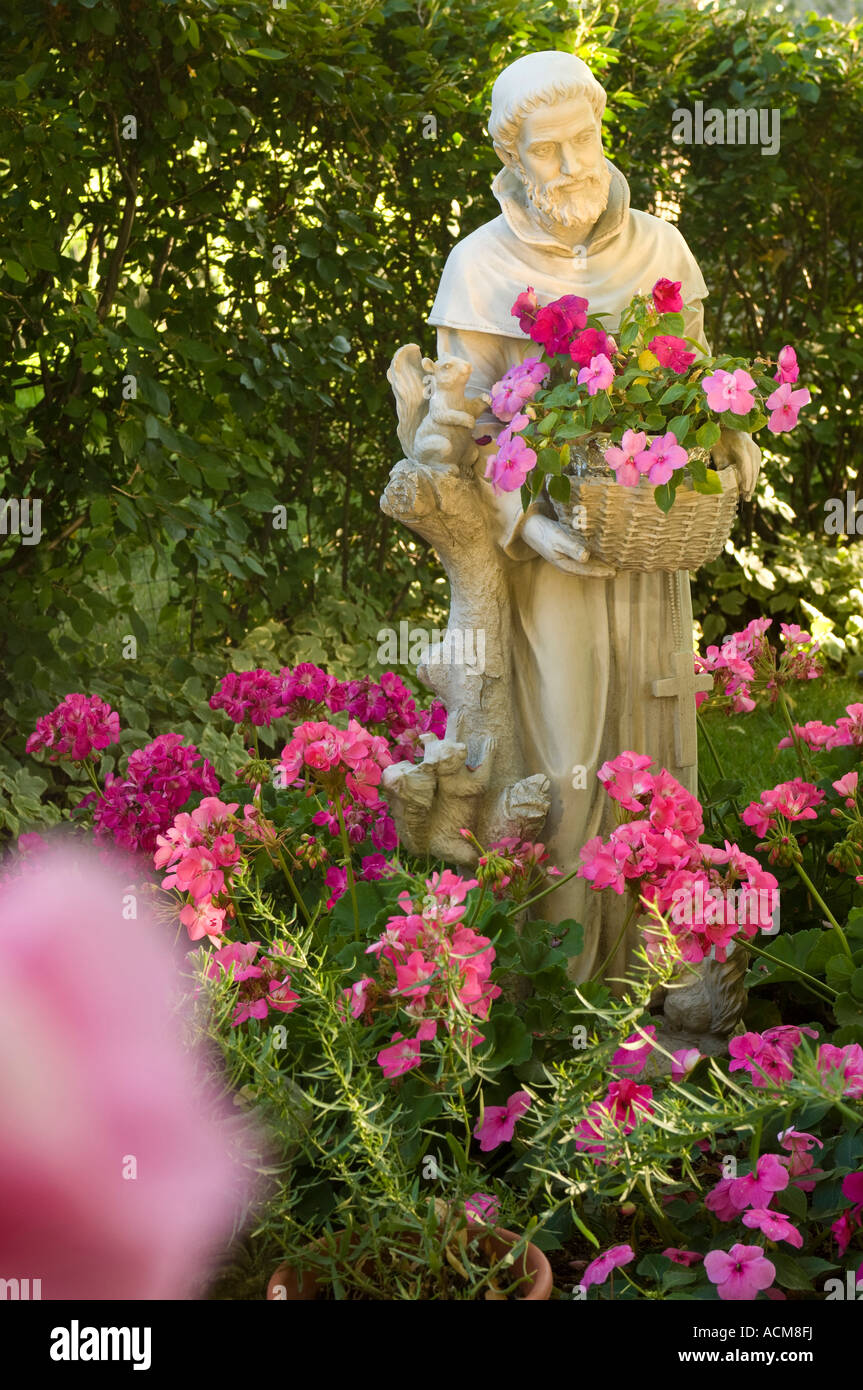 A STATUE OF SAINT FRANCIS PATRON SAINT OF ANIMALS STANDS IN A GARDEN OF  GERANIUMS AND IMPATIEN FLOWERS Stock Photo - Alamy