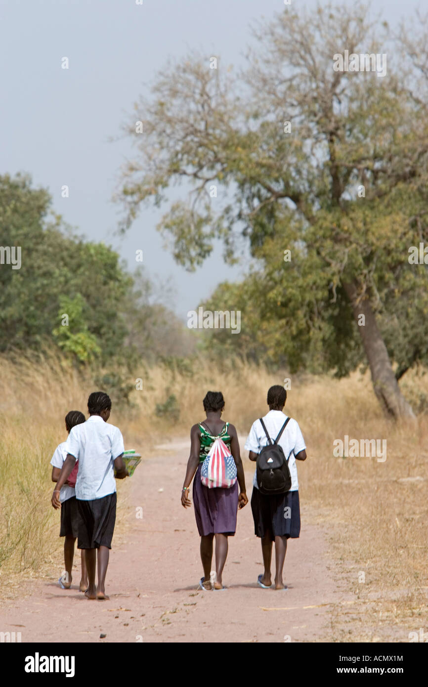 School girls in uniform with back packs walk home on dusty track near Tendaba The Gambia Stock Photo