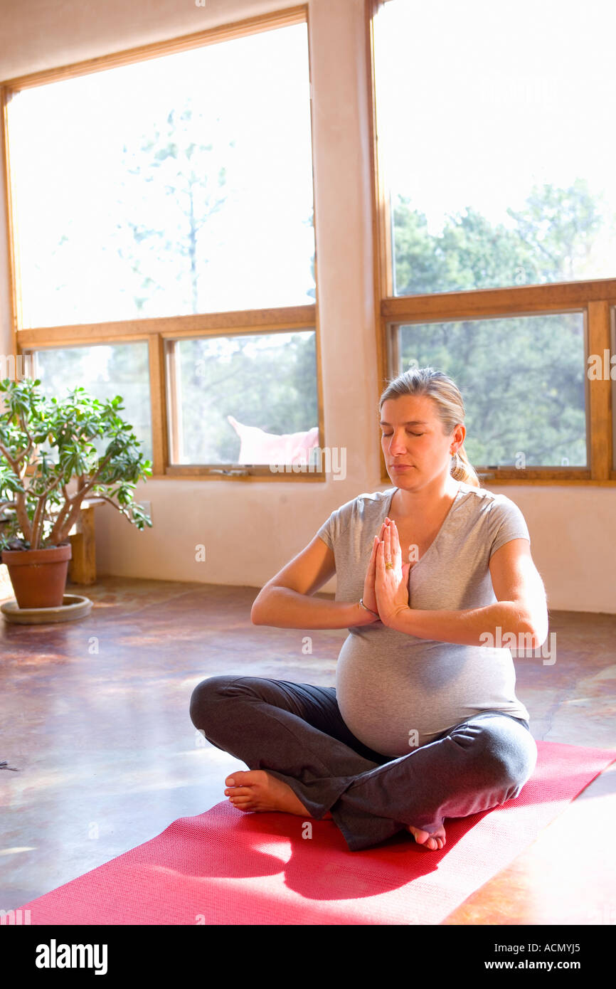 pregnant woman sitting cross-legged on mat doing yoga at home Stock ...