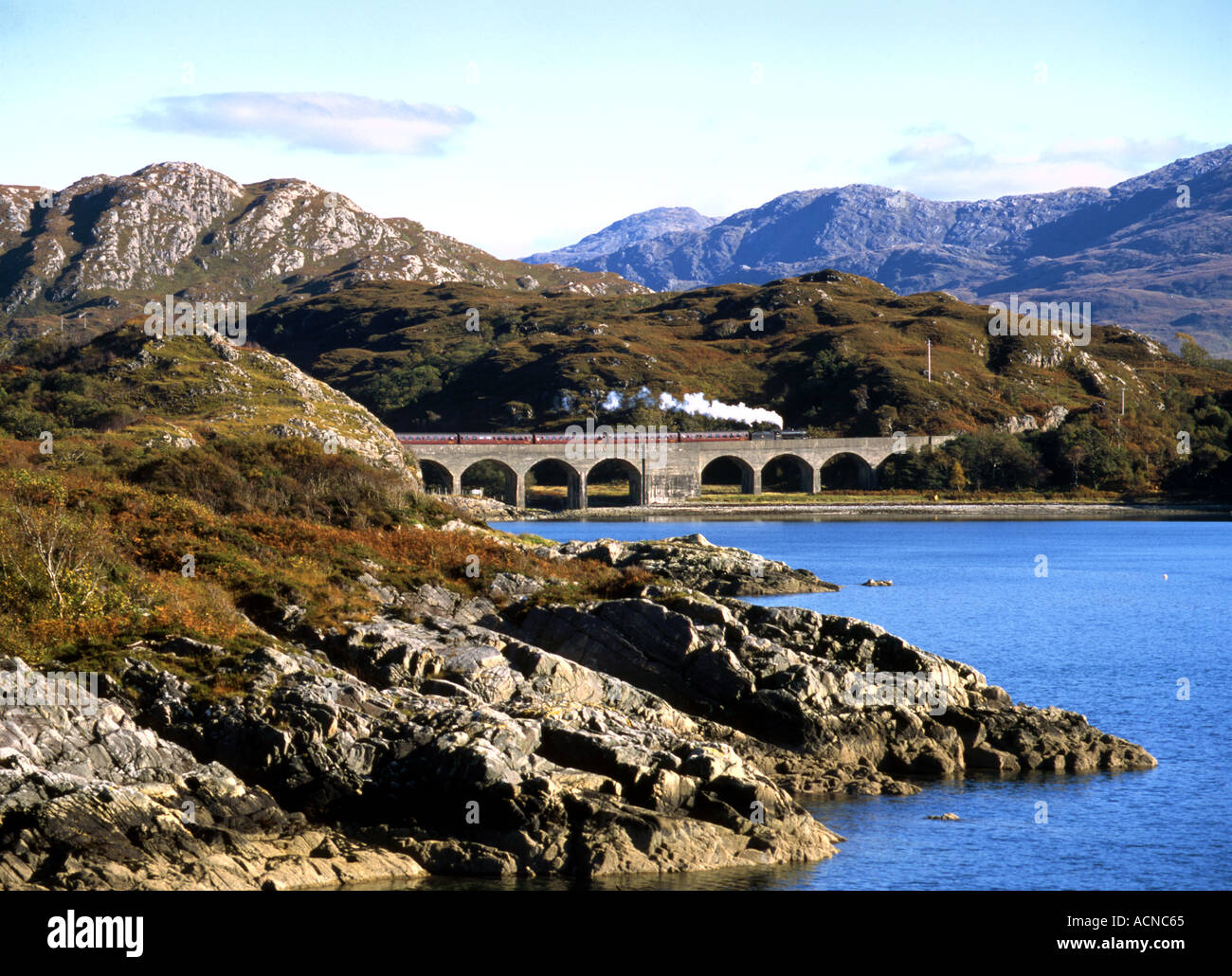 Steam train from Mallaig to Fort William passes over the Loch nan Uamh viaduct south of Arisaig Stock Photo