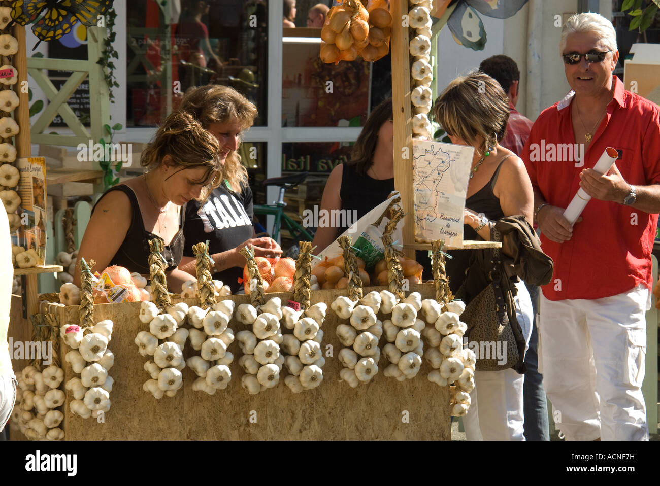 France. Beaumont de Lomagne. Women selling tresses of garlic in the market Stock Photo
