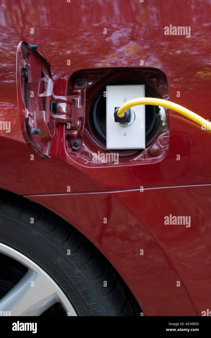 An electrical cord plugged into an outlet sitting inside the gas tank door of a car Stock Photo