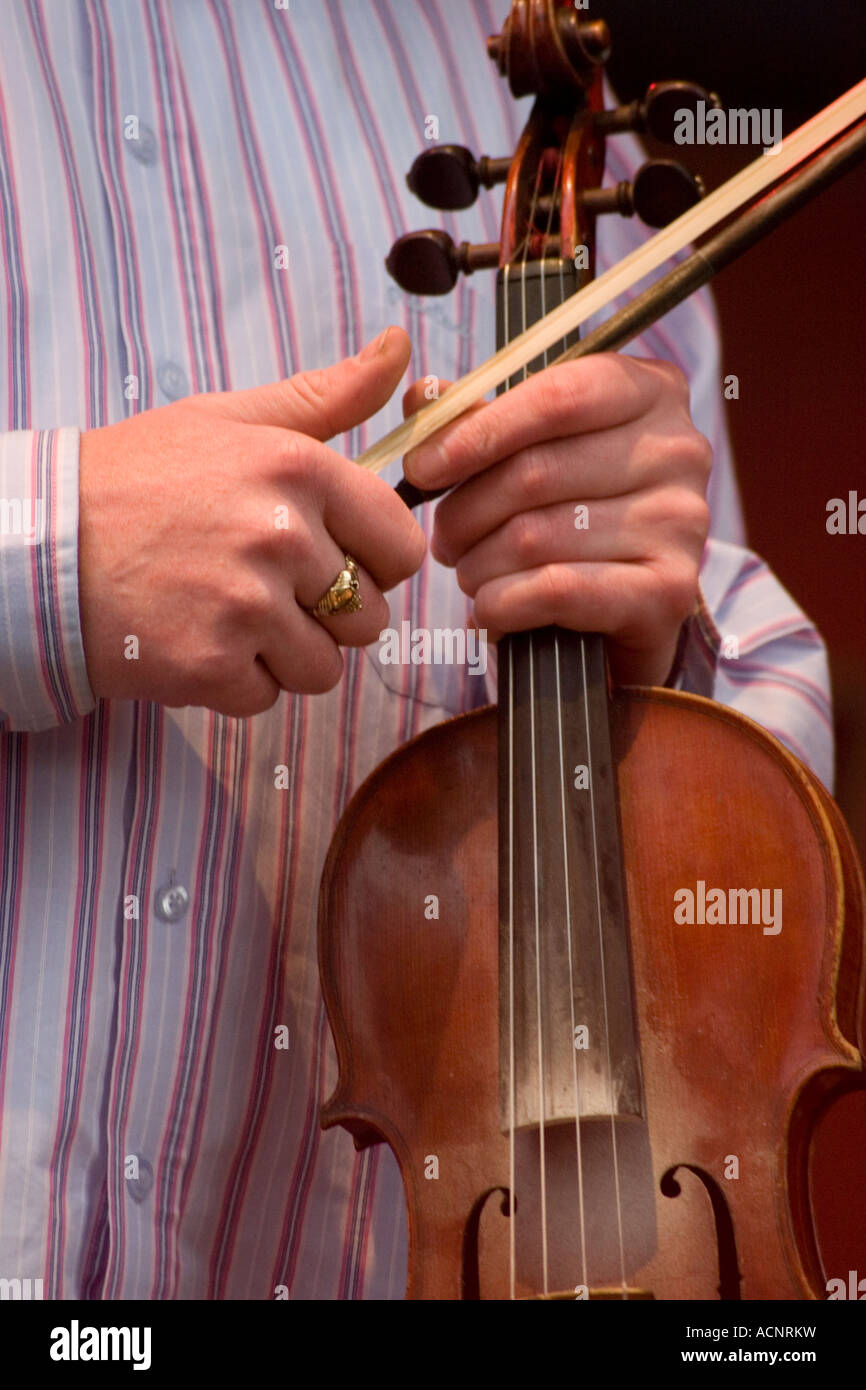 Man in striped shirt holding violin and bow on stage at Irish traditional music concert Stock Photo