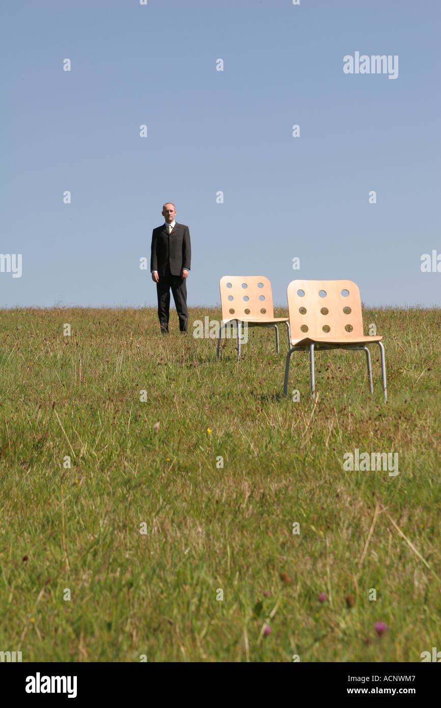 Businessman behind stools on the meadow - Geschäftsman hinter Stühlen auf der Wiese Stock Photo