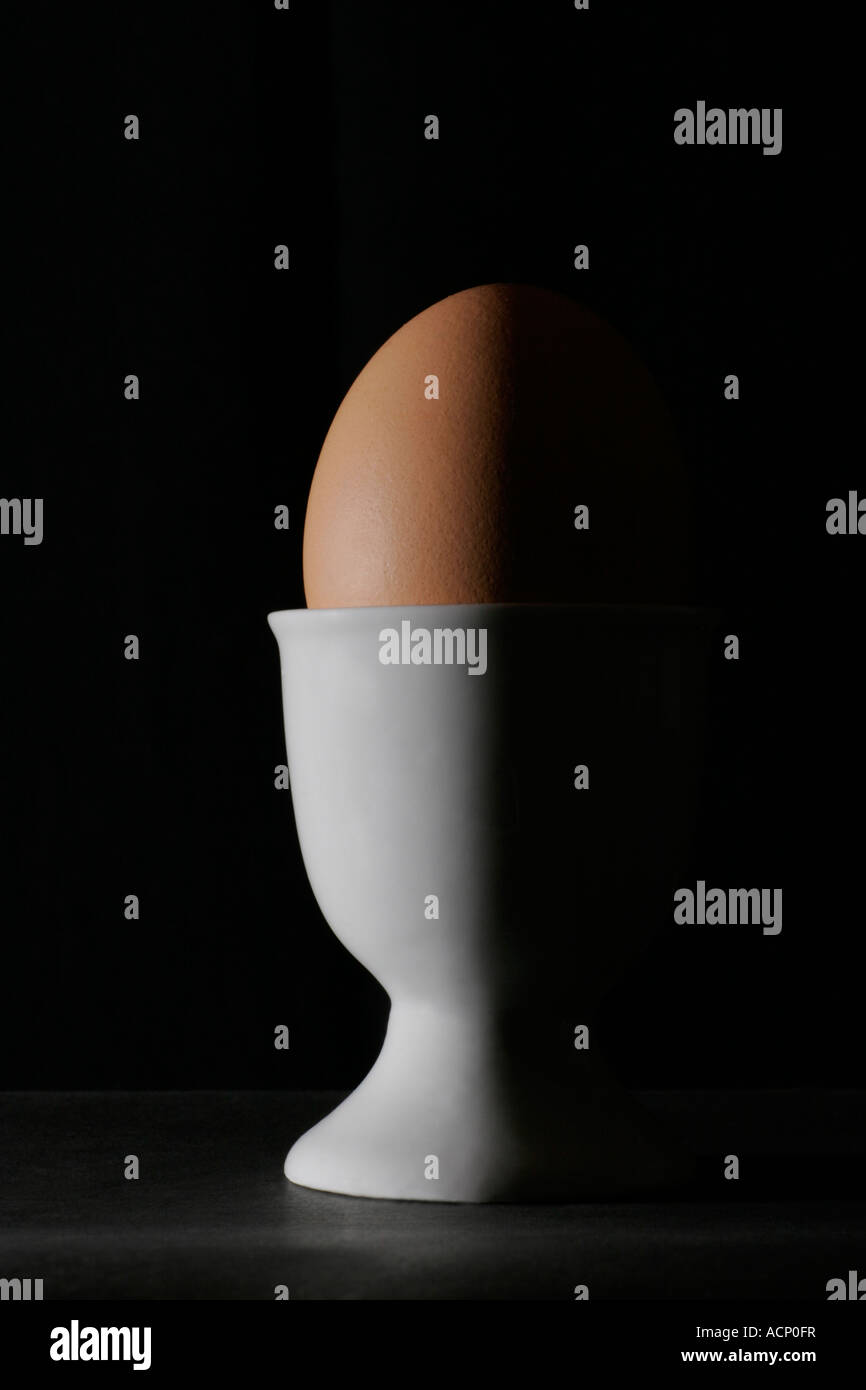Profile of a boiled egg in a white eggcup showing highlights against a black background Stock Photo