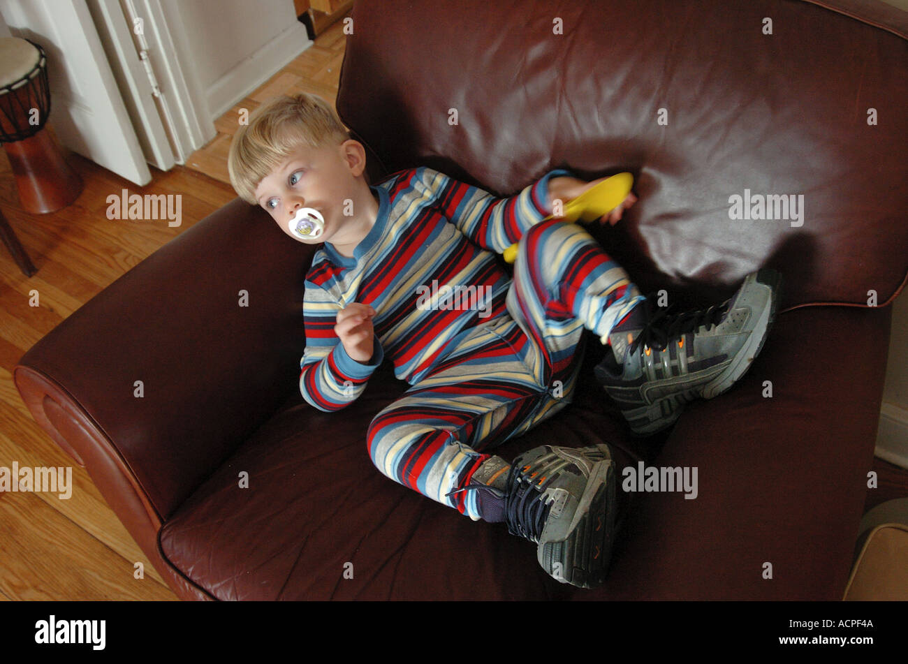 baby humor child laying in chair wearing big sneakers Stock Photo