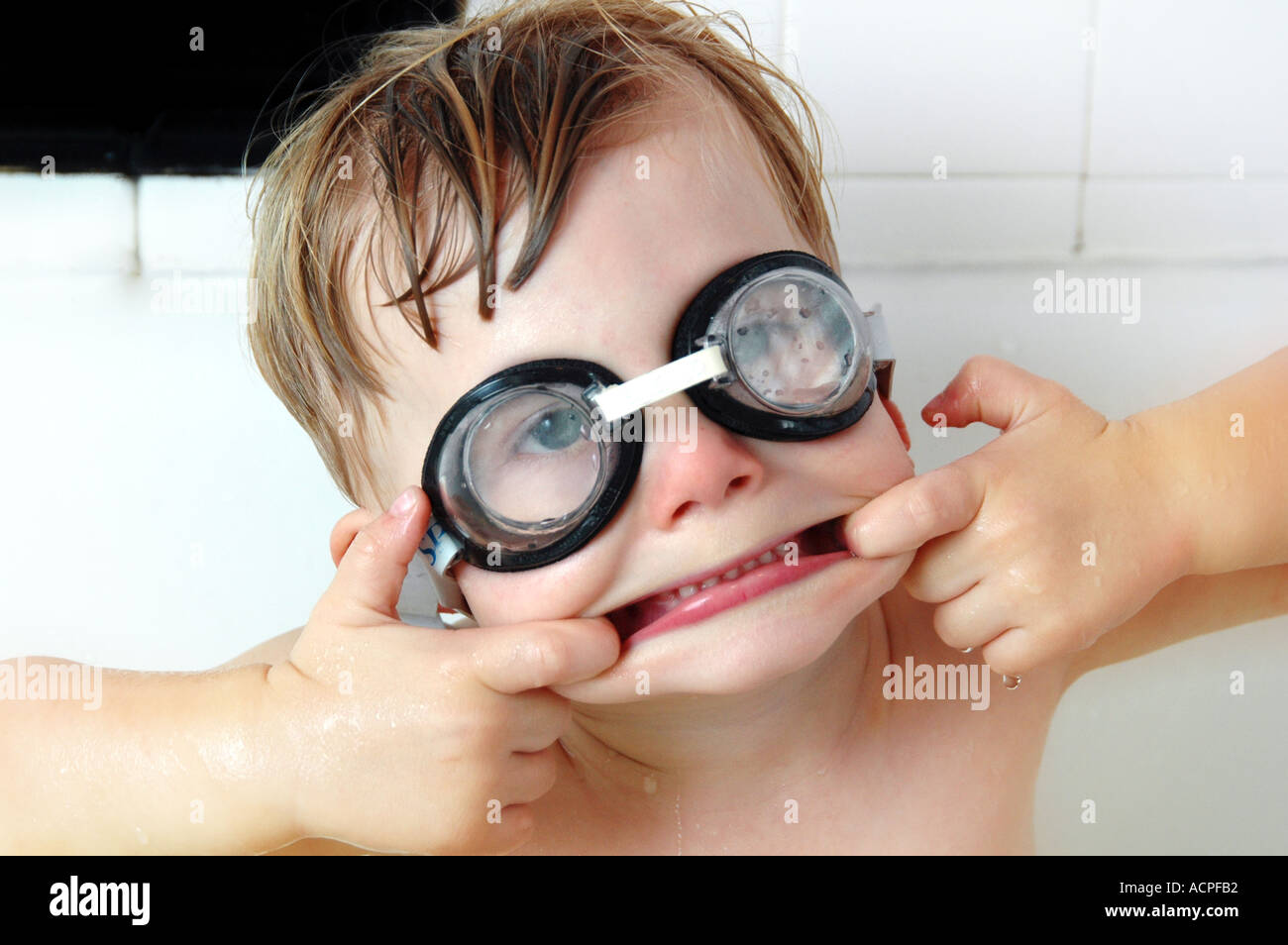Small boy in tub wearing swimmers goggles making funny face smiling laughing humor humour family life Stock Photo