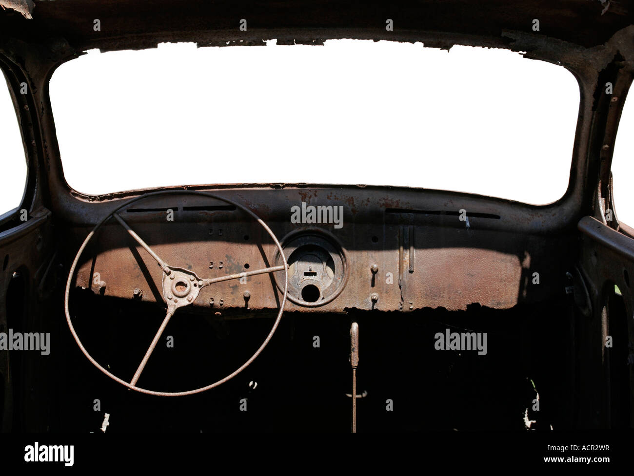 Inside of an old rusty wreck of a car showing dashboard and steering wheel with the windscreen isolated white. Stock Photo
