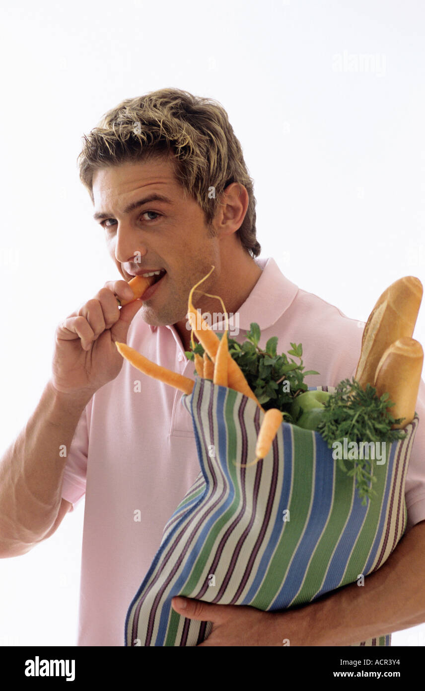 Man carrying grocery bag, eating carrot Stock Photo