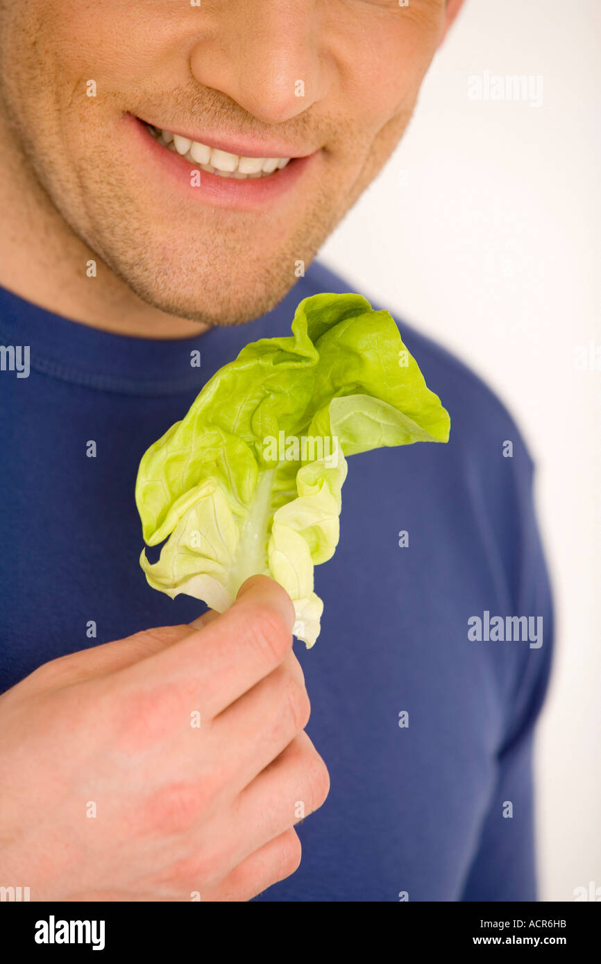 Young man holding lettuce leaf, smiling, close-up Stock Photo