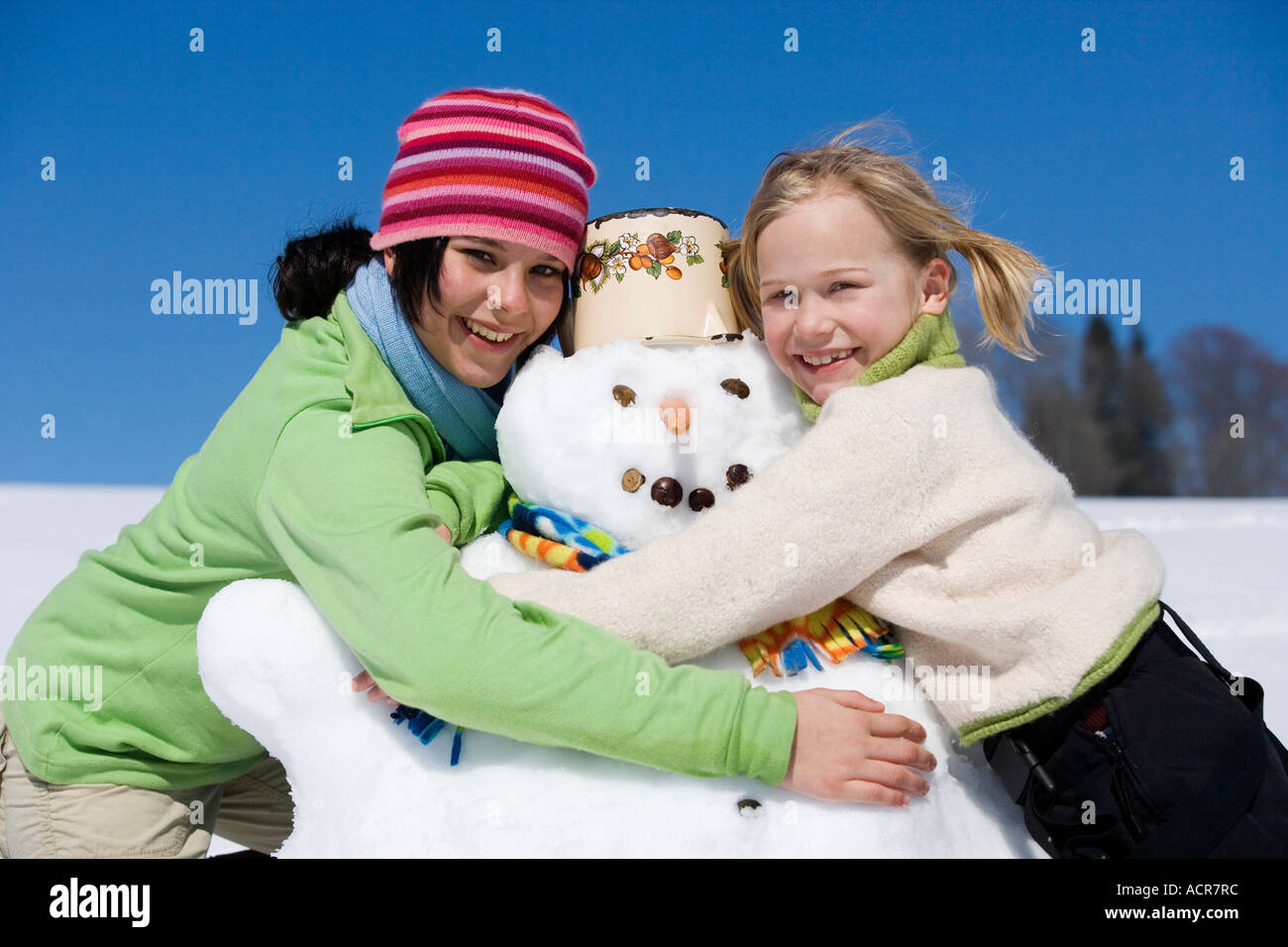 Austria, girls (6-17) hugging snowman, smiling, portrait Stock Photo