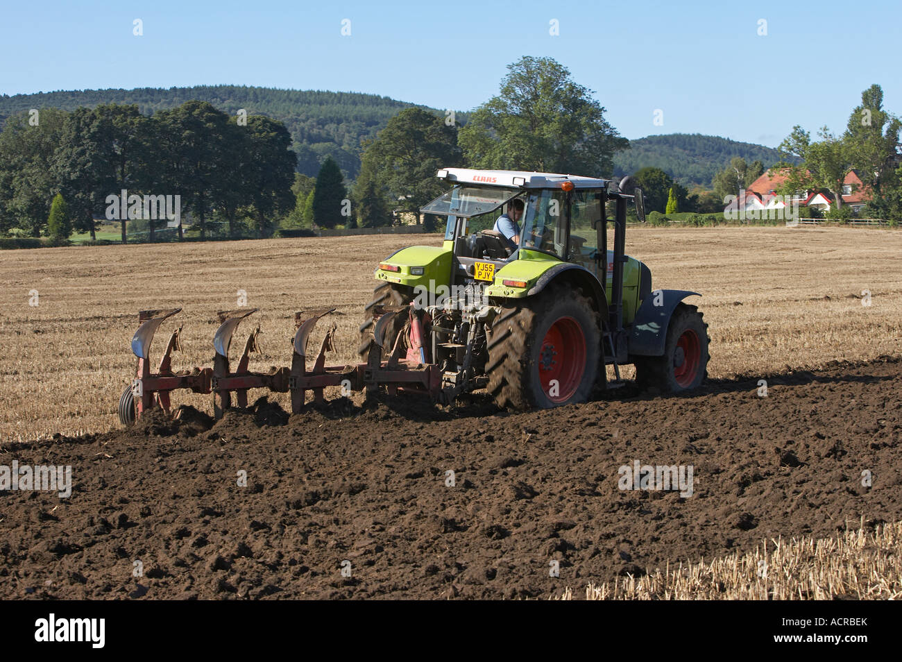 Green Claas tractor towing mounted plough (stubble ploughing, turning soil & mud, preparing land, farm worker driving) - West Yorkshire, England, GB. Stock Photo