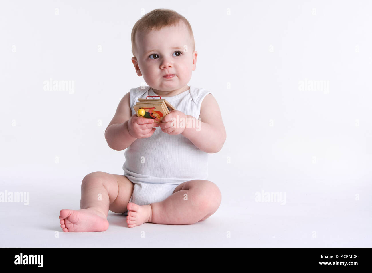Little baby sitting on the floor with a wooden toy book Stock Photo - Alamy
