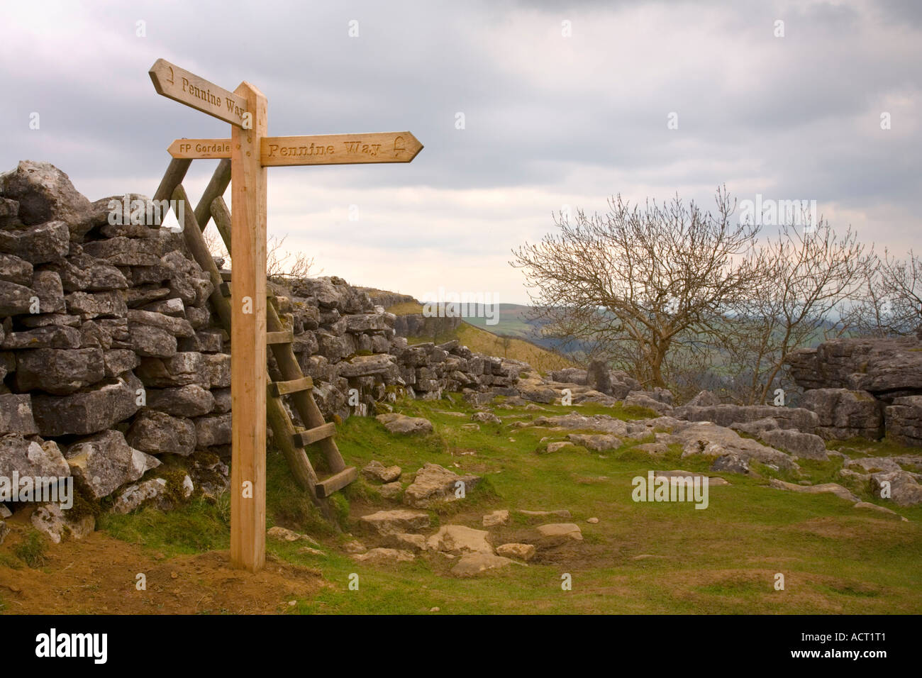 A new wooden sign on the Pennine Way in Yorkshire England at Malham Cove Hikers visible in the distance Stock Photo