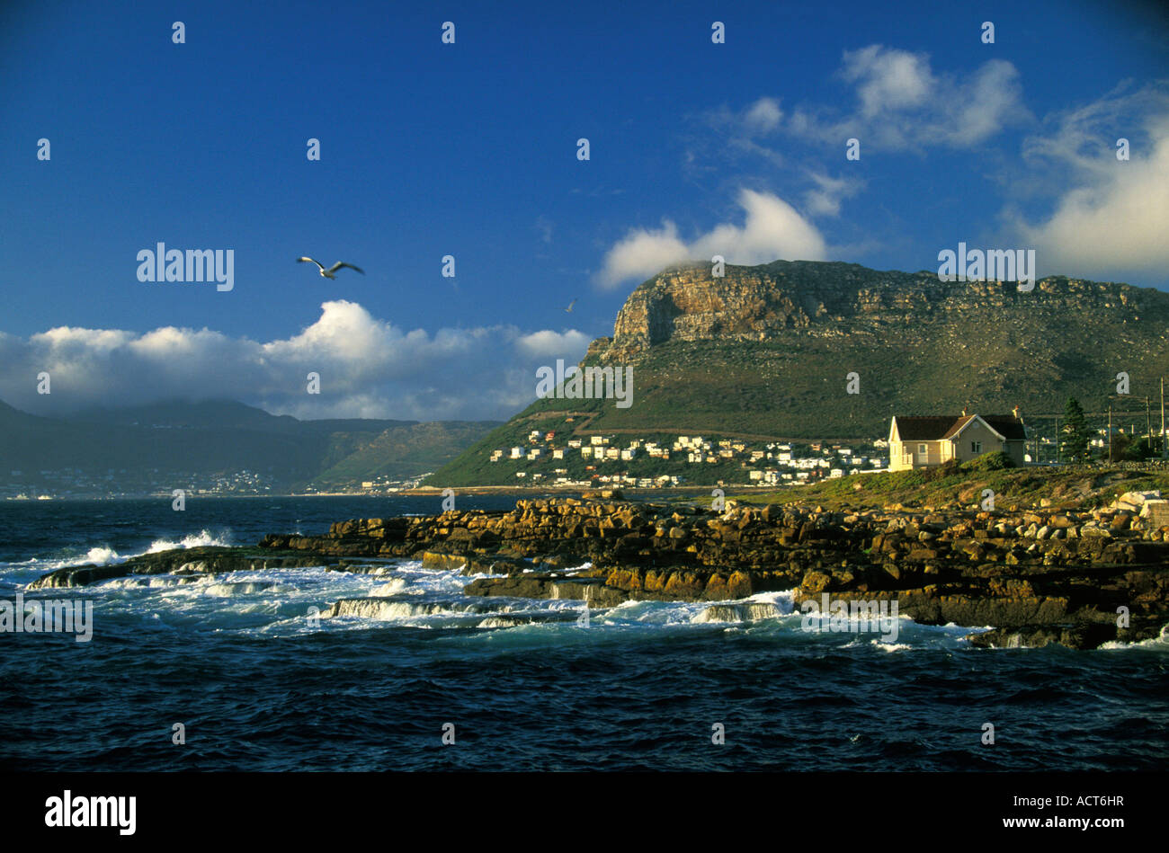 A view over a rocky beach with holiday homes on the slopes of a hill in the background Western Cape South Africa Stock Photo