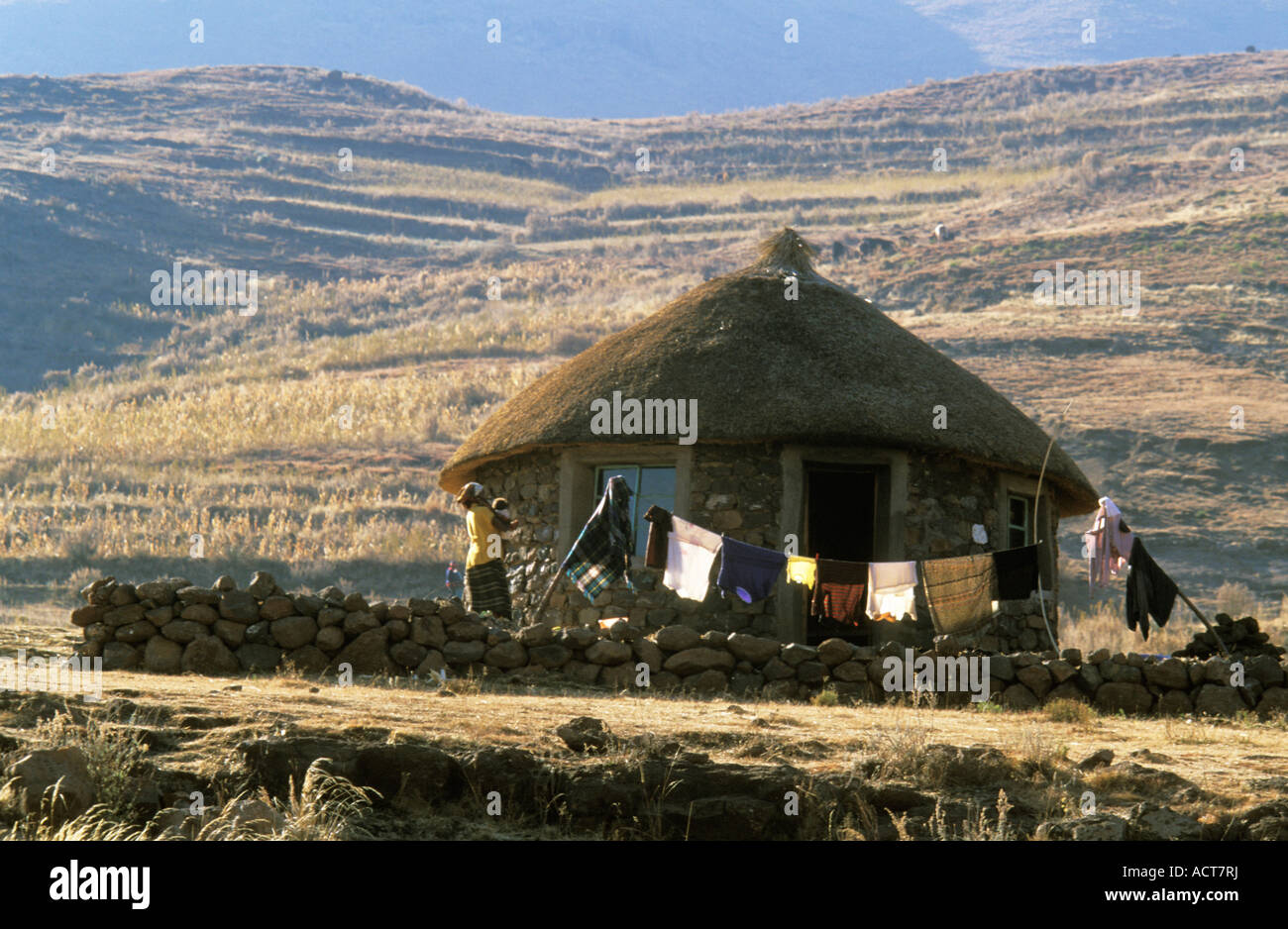 Traditional stone and thatch homestead with makeshift wash line built at the base of a hillside Lesotho Stock Photo