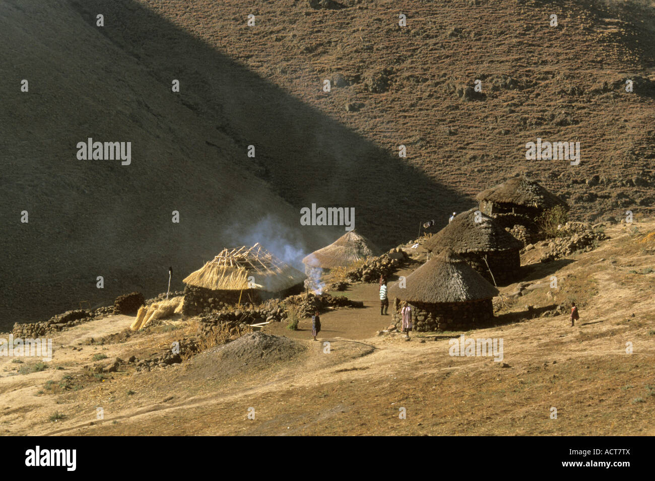 Traditional stone and thatch homesteads built on a hillside sloping down to an enclosed valley Lesotho Stock Photo