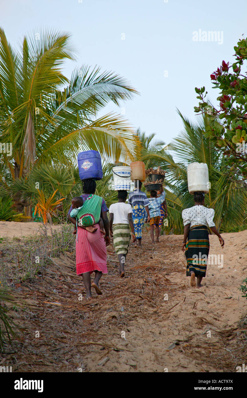 Women one with a child on her back carrying water collected from a coastal well to their homes Barra Mozambique Stock Photo