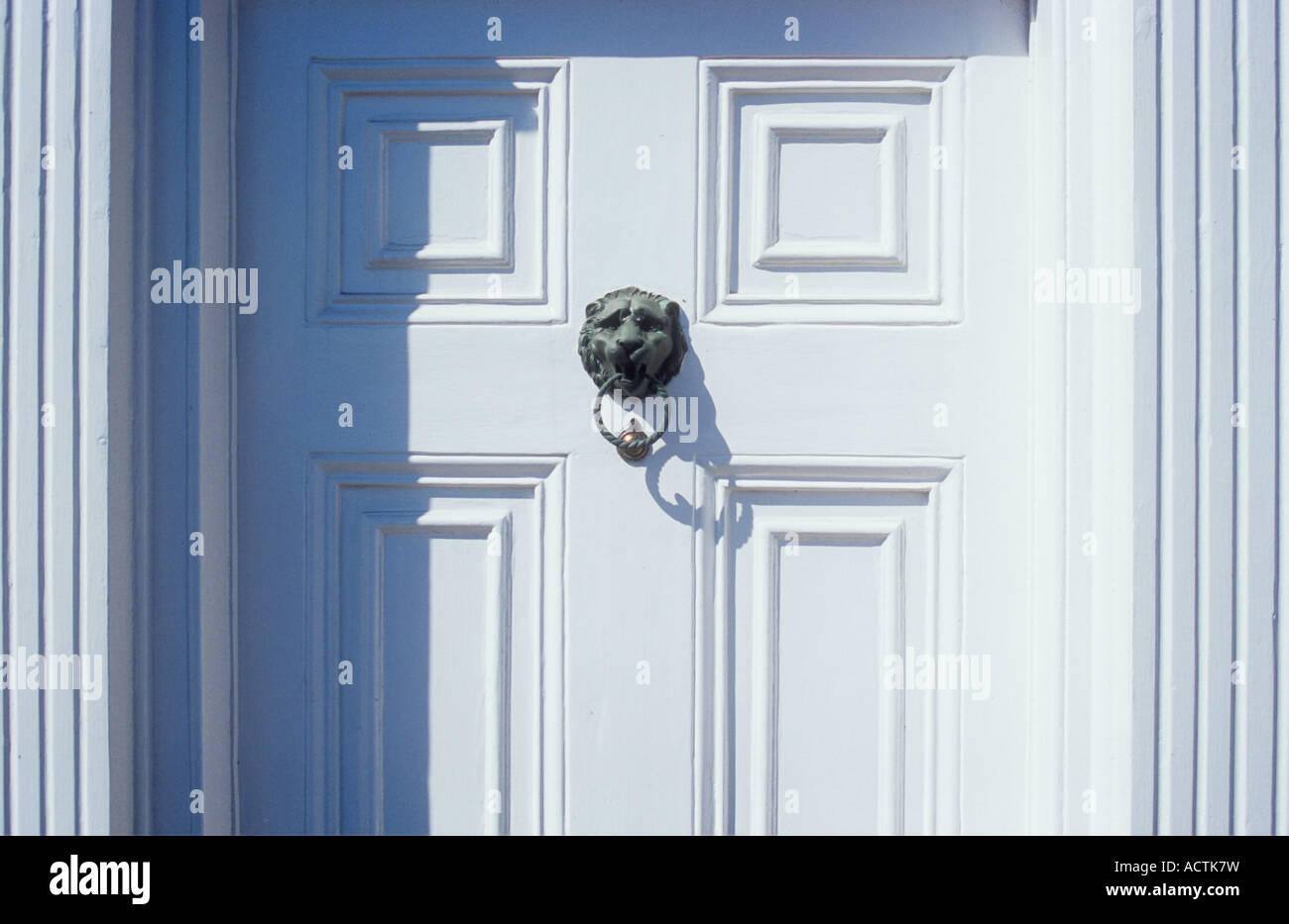 Stylish panelled front door and ribbed jambs freshly painted white with tarnished copper lion head knocker casting shadow Stock Photo