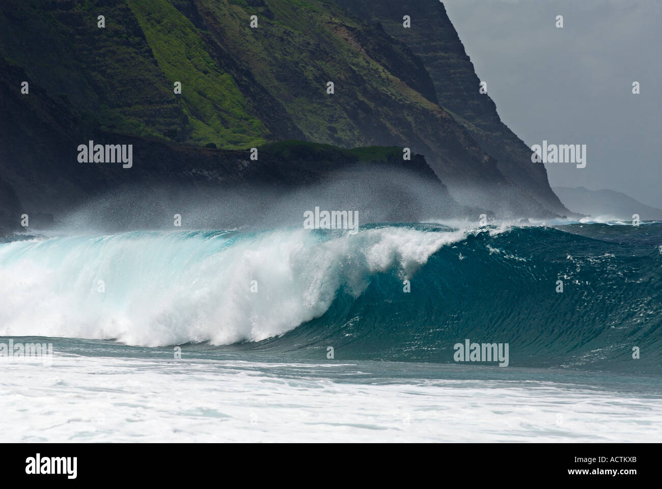 Salt spray of wave breaking on Kalaupapa leper colony beach with steep cliffs on Molokai Hawaii Stock Photo