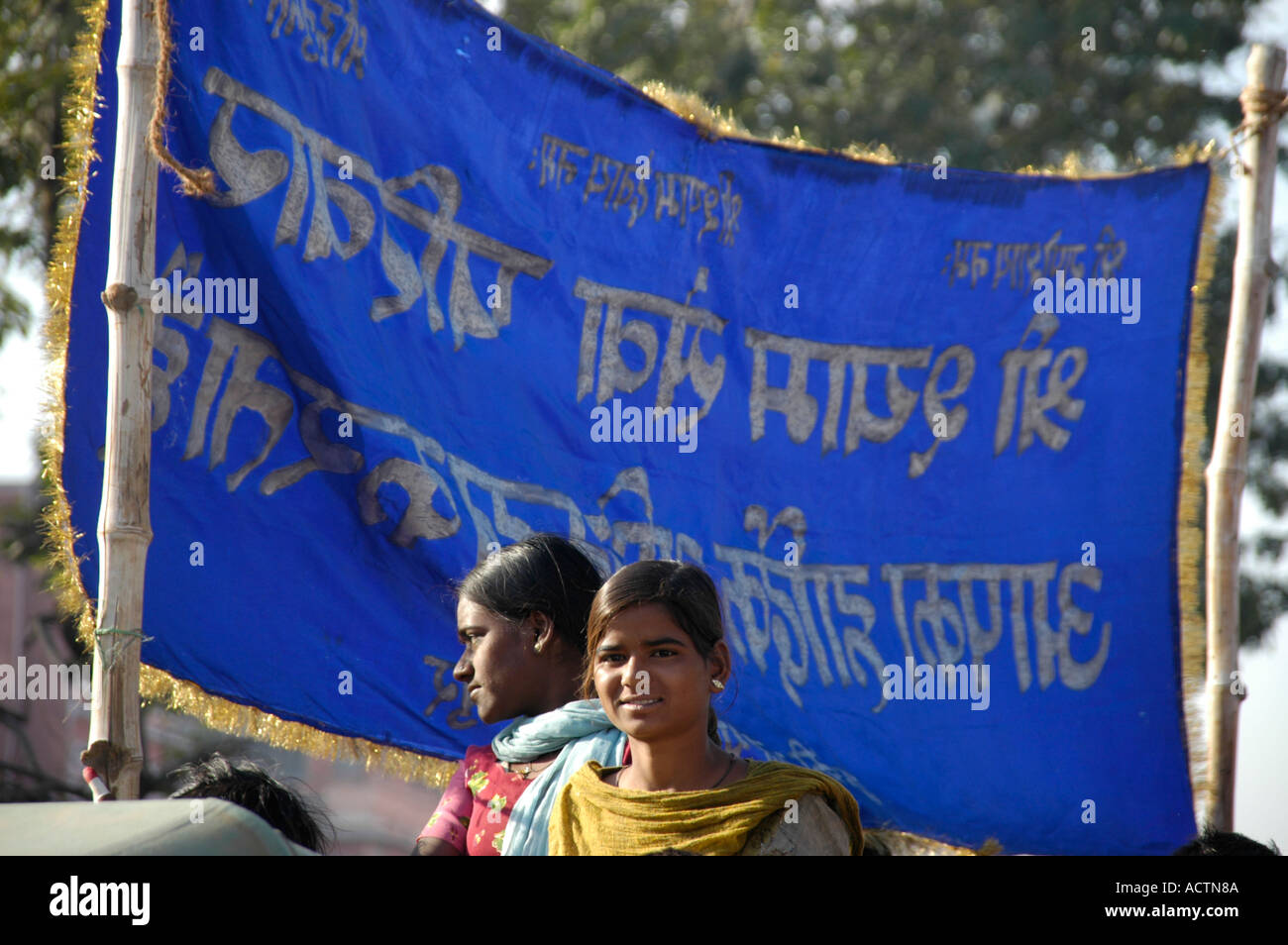 Two young Indian women in front of a blue flag with Indian script ...