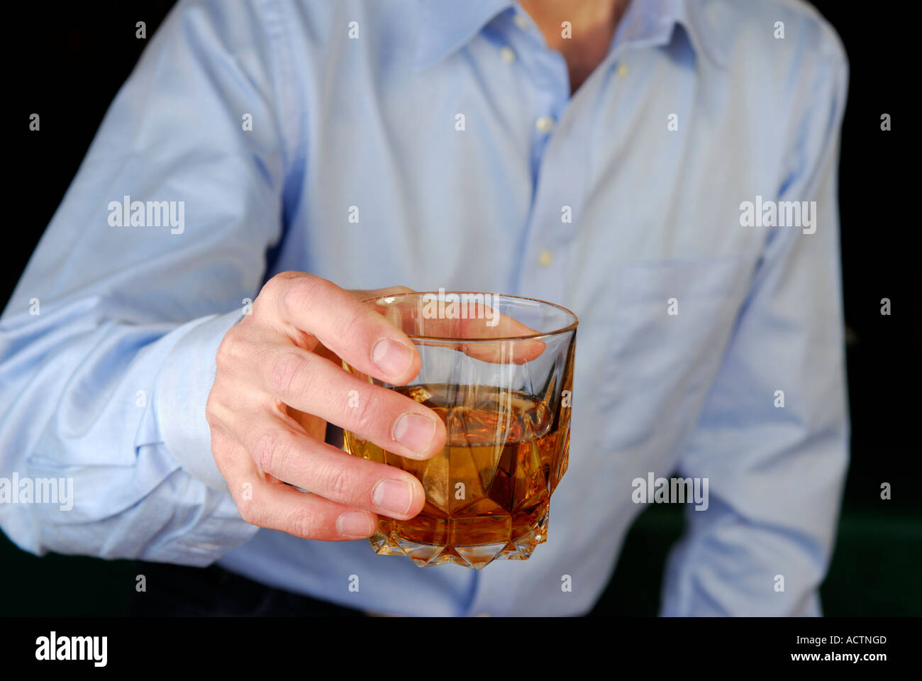 Man holding out a glass offering whiskey alcohol  to say cheers Stock Photo