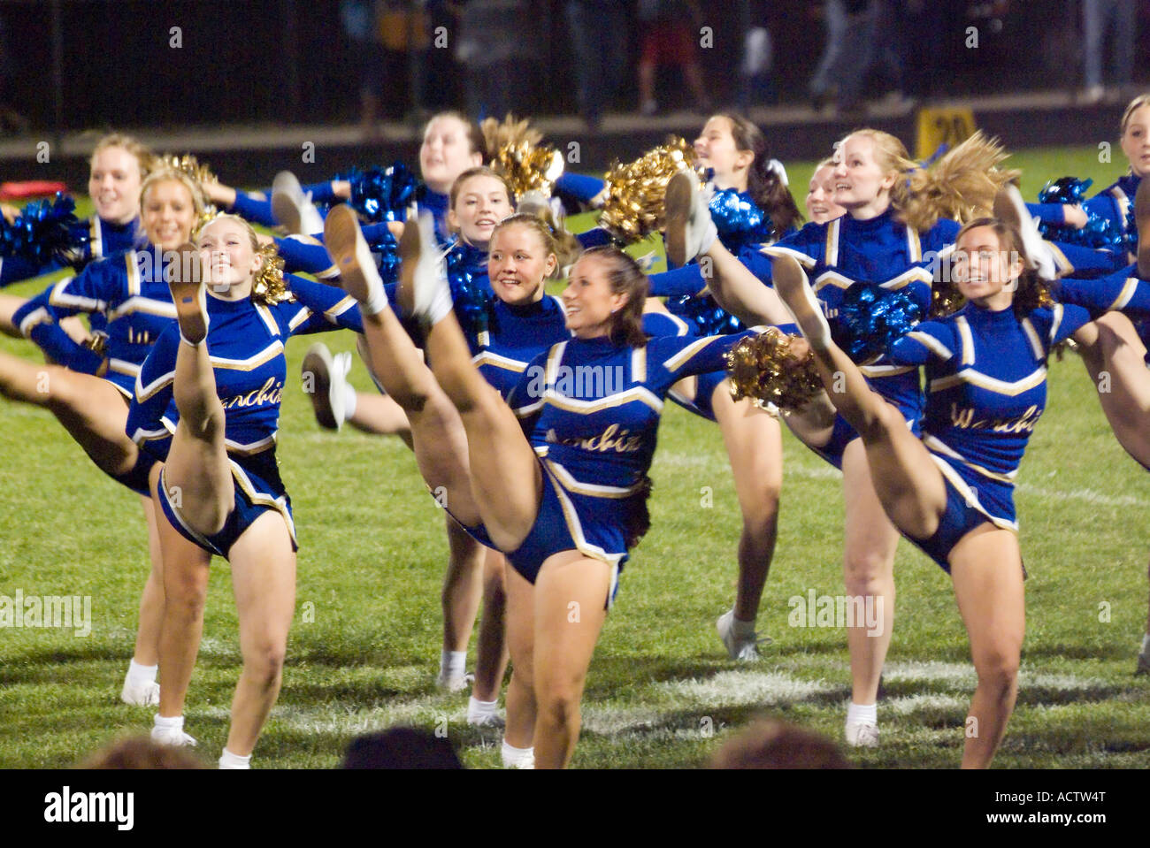 CHEERLEADERS DRESSED IN BLUE ARE PERFORMING IN SYNC ON A HIGH SCHOOL FOOTBALL GAME Stock Photo