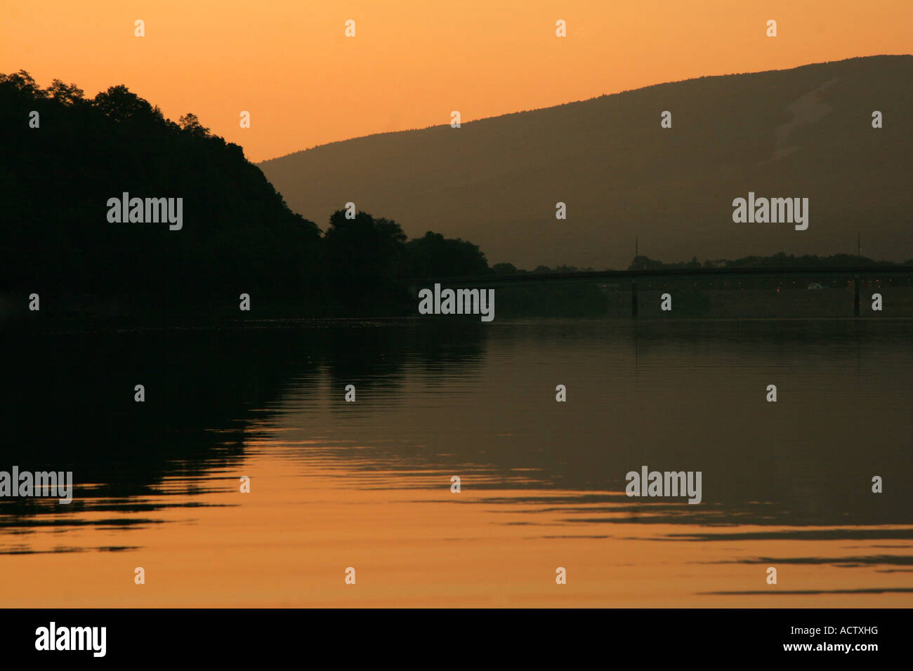 Bright orange sunrise over river with trees and hills reflecting. Stock Photo