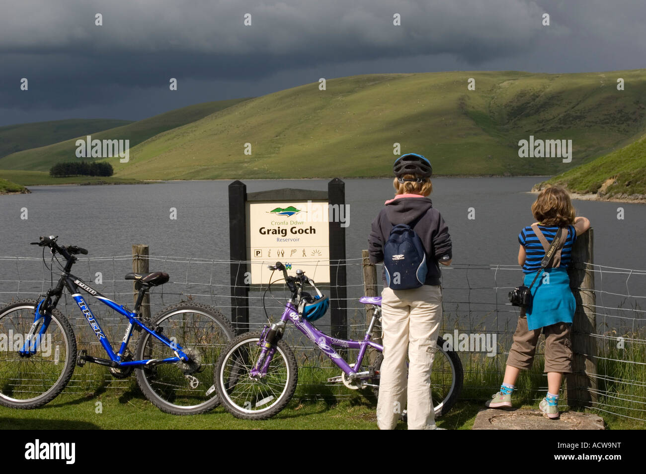 Two young girls with bicycles standing by Craig Goch reservoir and dam Elan Valley Trail , Powys mid Wales UK Stock Photo