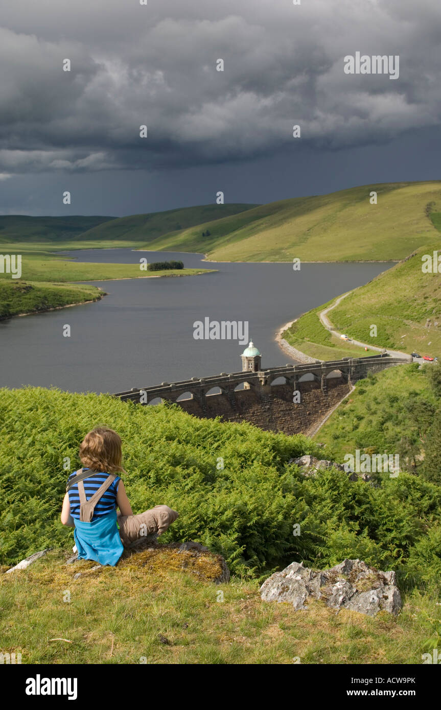 young girl sitting down looking at the Graig Goch reservoir and dam Elan Valley Powys mid Wales Stock Photo