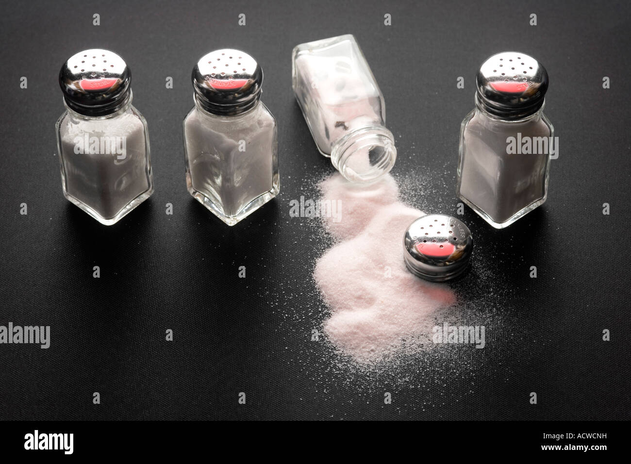 Four salt shakers in a table with spilled salt Stock Photo Alamy