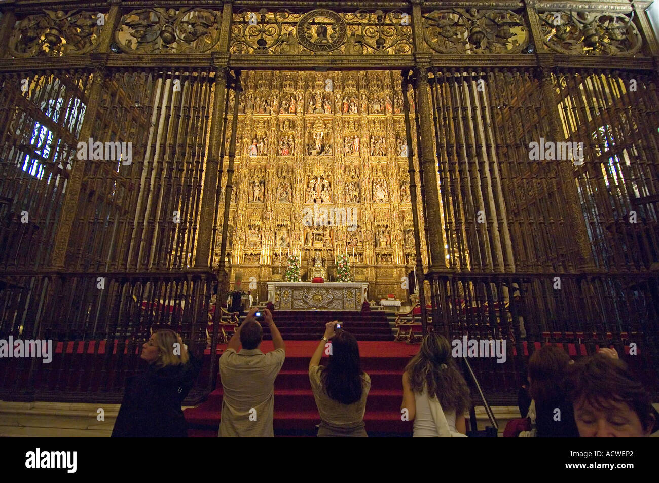 Visitors holding up cameras mimic supplicant pilgrims at the golden altarpiece in Seville cathedral - Andalusia, Spain Stock Photo