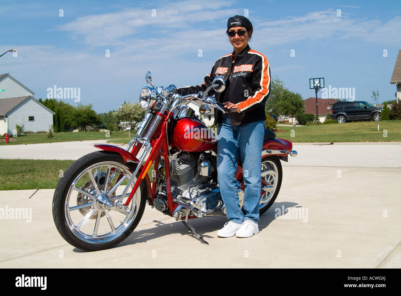 A HARLEY RIDER GIRL DRESSED IN HARLEY GEAR IS STANDING PROUDLY WHILE ...