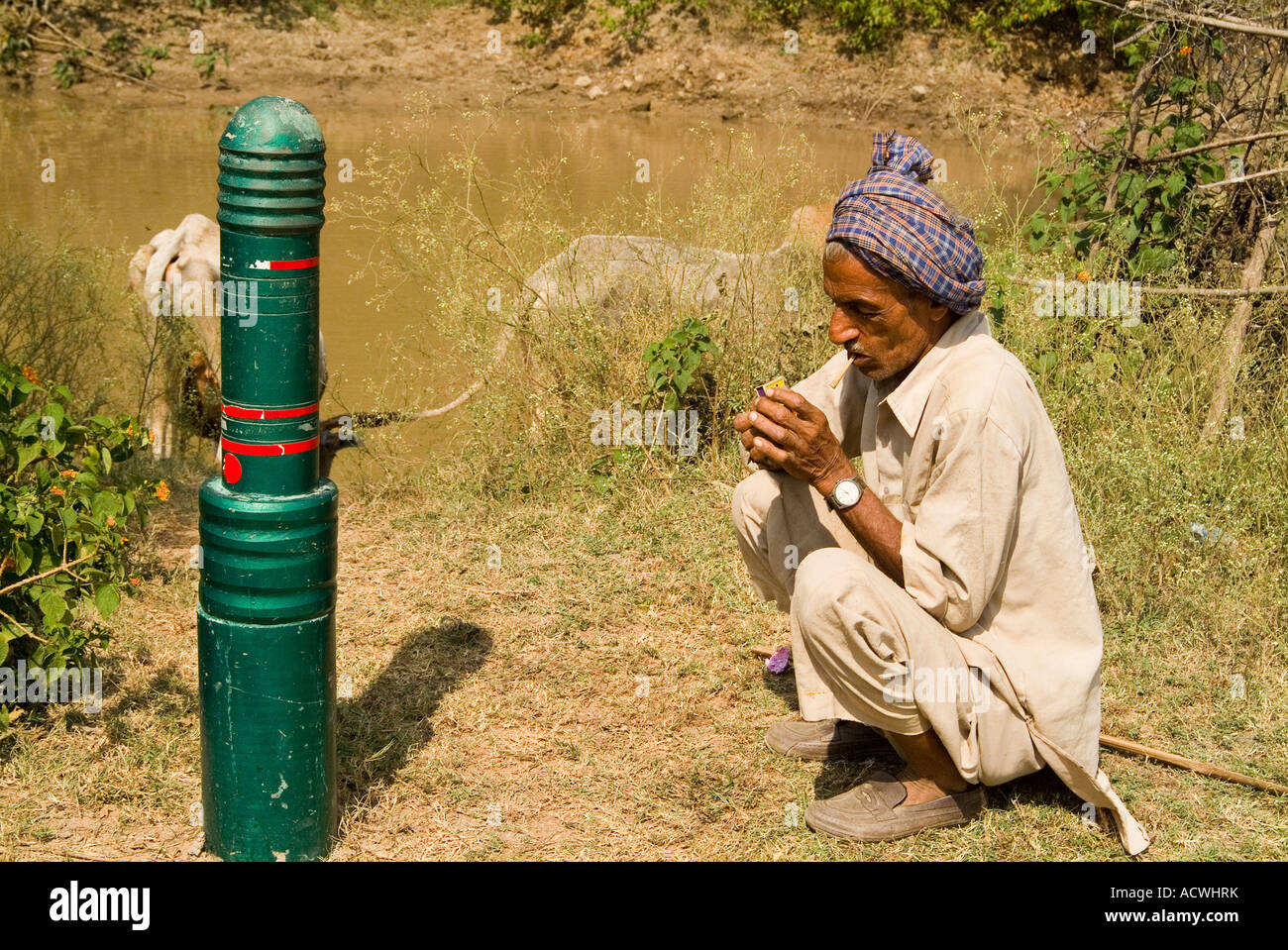AN INDIAN FARMER IS SQUATTING AND LIGHTING HIS CIGARETTE WHILE HIS