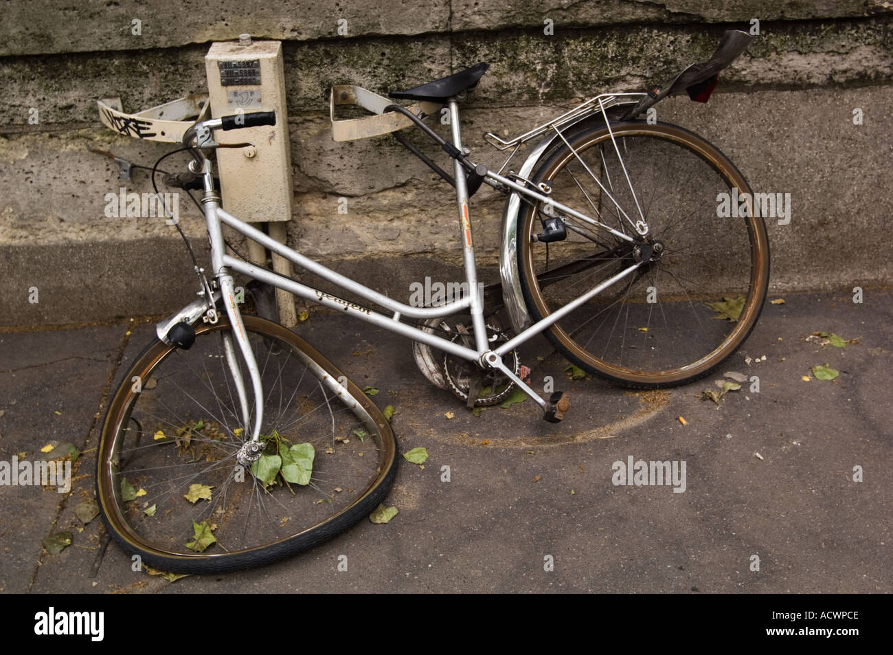 Color horizontal image of a damaged silver bicycle locked to a fixture on a sidewalk in Paris France Stock Photo
