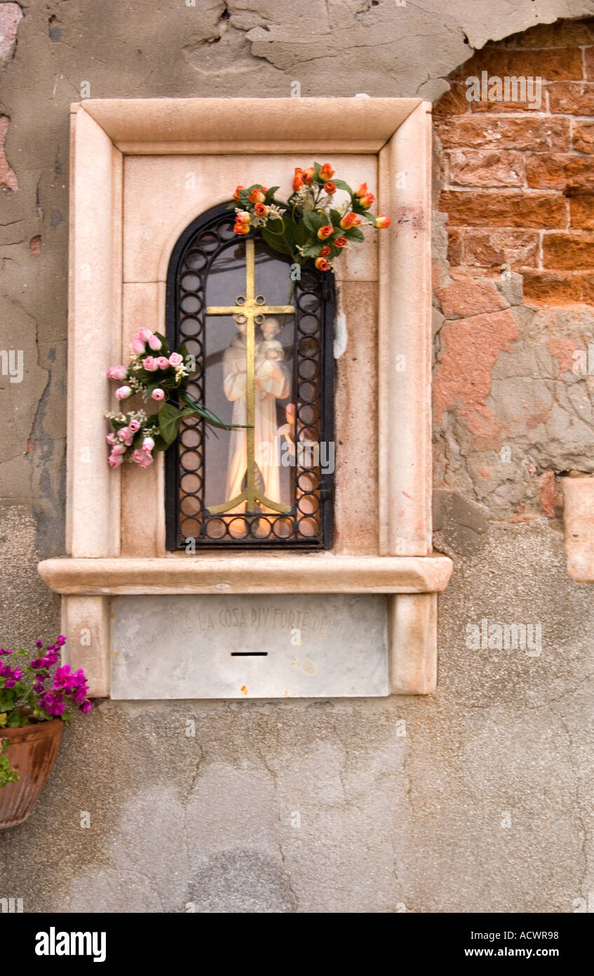 Color vertical image of a Catholic shrine in a brick wall lit behind glass and a cross with flowers in Venice Italy Stock Photo
